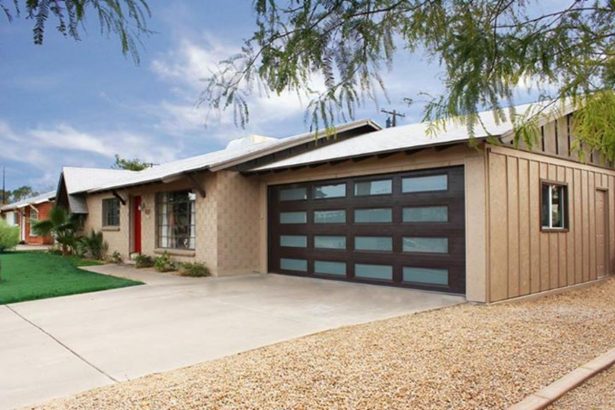Single-story beige stucco house with dark modern glass-paneled garage door and gravel driveway